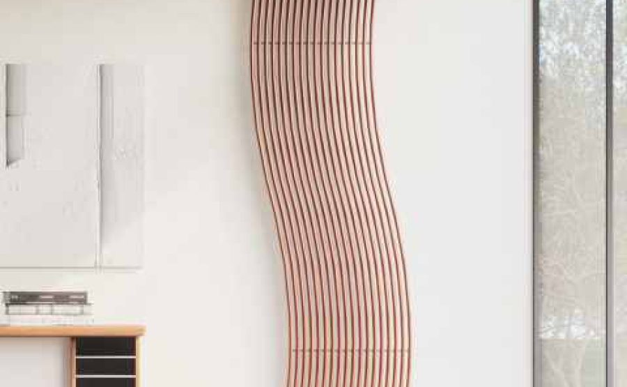 Radiatore verticale curvo in finitura rame installato su parete bianca in un ambiente moderno.