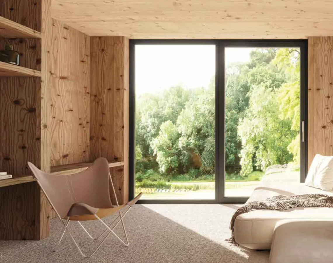 Zona living con pareti in legno scuro e vetrata su bosco