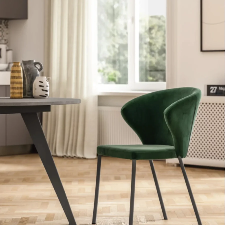 Sedia moderna in velluto verde con gambe nere metalliche, in ambiente luminoso.