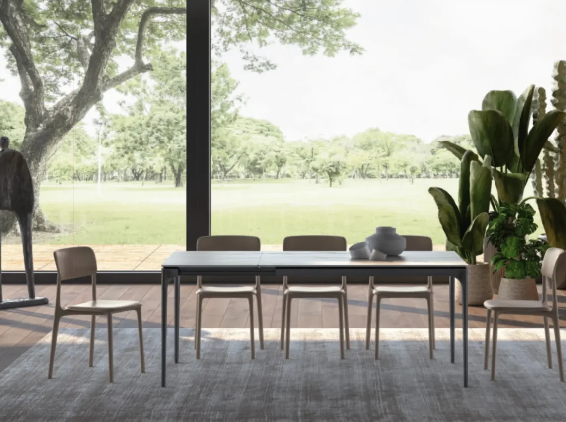 Tavolo Easyline estensibile con sedie beige, collocato in un ambiente con vetrata sul giardino.