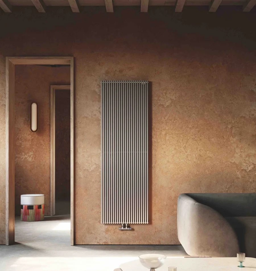 Radiatore verticale grigio chiaro installato su parete color terra cruda in soggiorno moderno con arredi curvi.