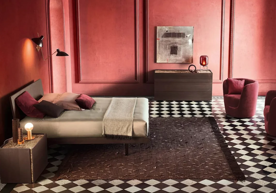 Letto moderno con testiera inclinata in tessuto beige, ambientato in una camera dai toni rosso scuro.