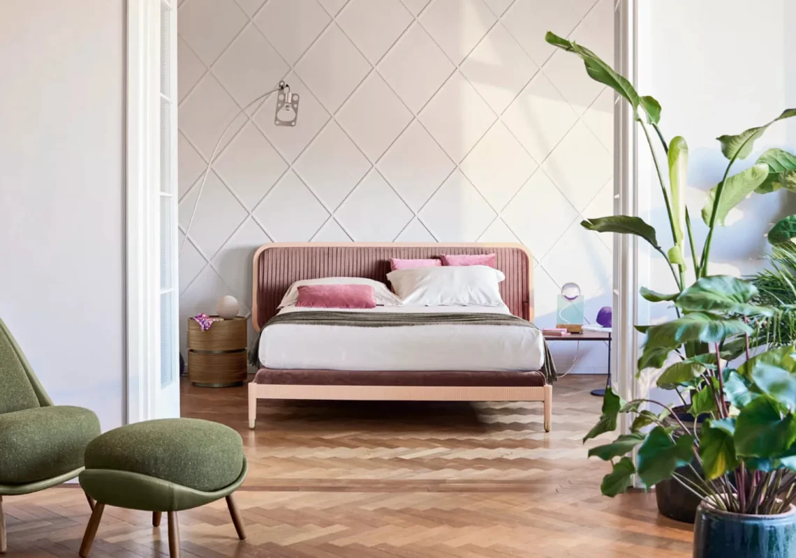 Letto con testiera arrotondata e rivestimento in tessuto rosa, ambientato in una stanza luminosa con parquet.