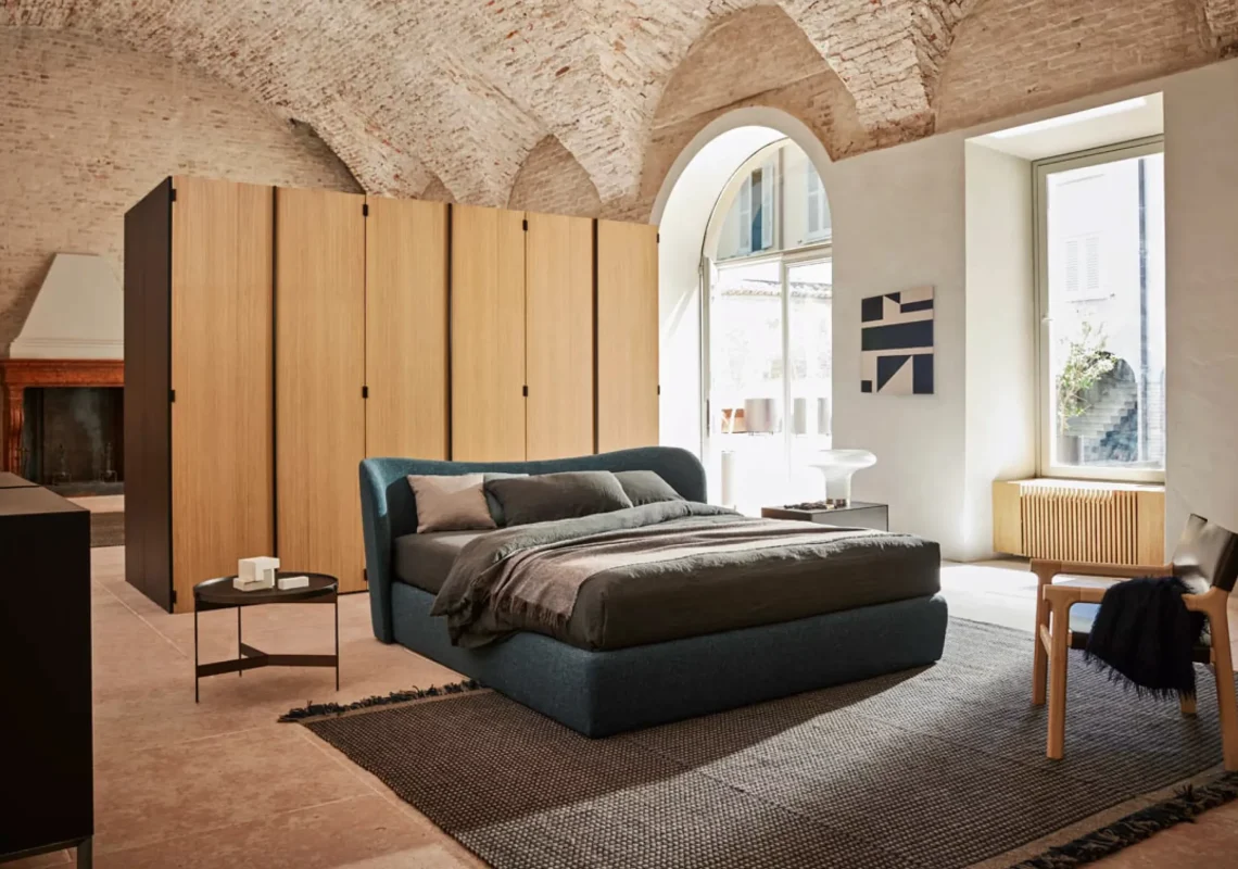 Letto imbottito blu petrolio con testiera arrotondata in stanza con soffitto a volta.