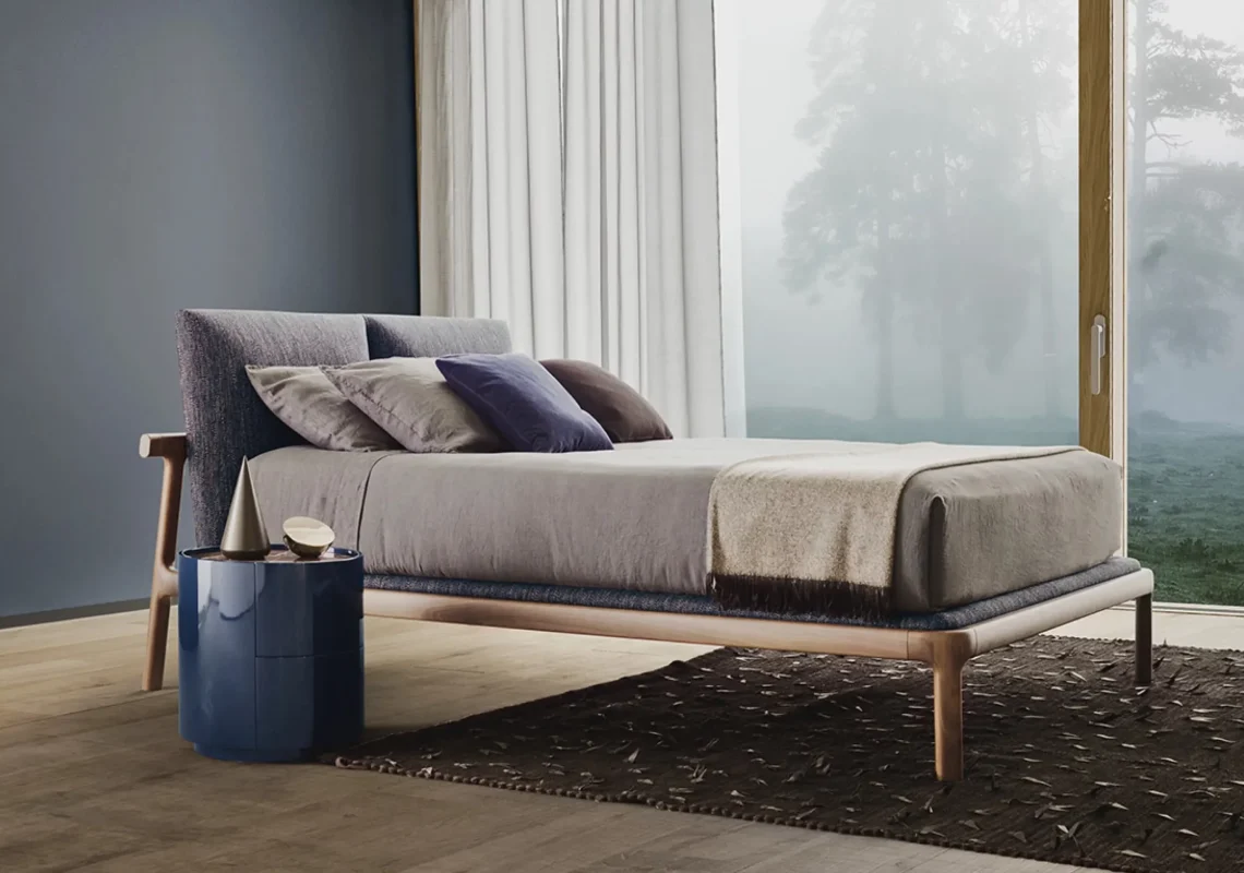 Letto in tessuto grigio chiaro con struttura in legno, in camera dai toni neutri.