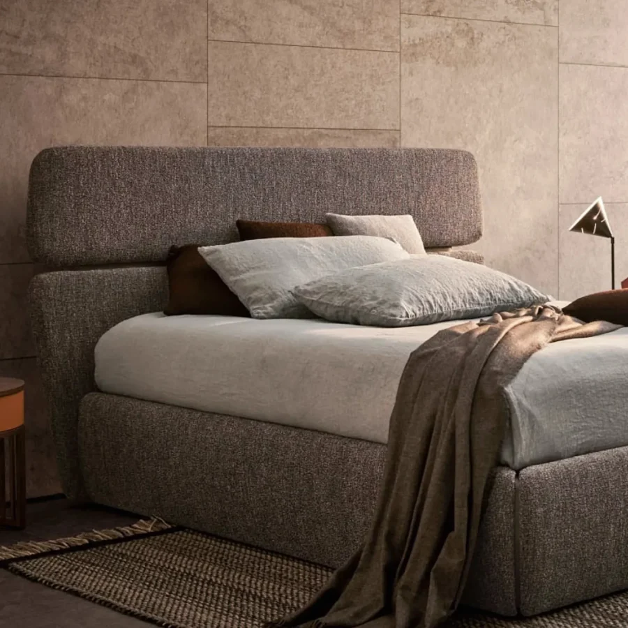 Camera da letto con letto imbottito grigio e comodino rotondo in legno scuro con cassetto cuoio