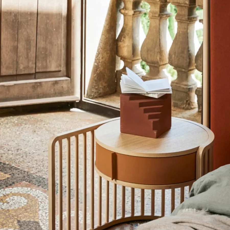 Tavolino rotondo con struttura in legno scuro e lampada da lettura moderna in primo piano.