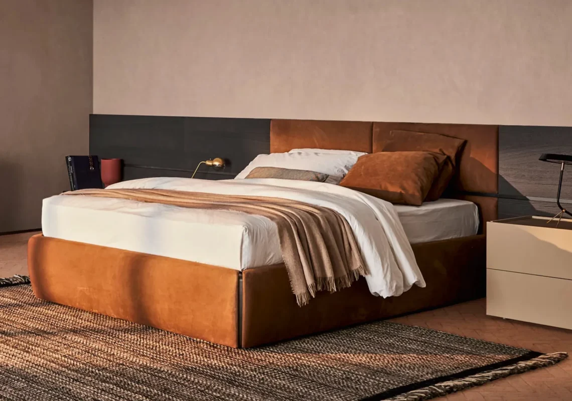 Letto rivestito in pelle color cuoio con testiera imbottita in una camera calda e moderna.
