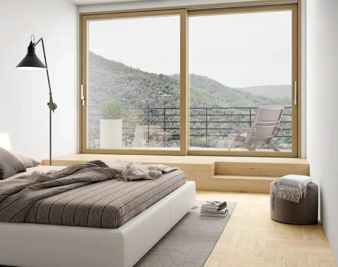 Camera da letto con vetrata scorrevole in legno chiaro affacciata su balcone con vista collinare