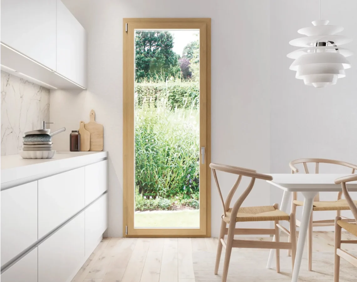 Cucina luminosa con porta finestra in legno chiaro affacciata su giardino verde
