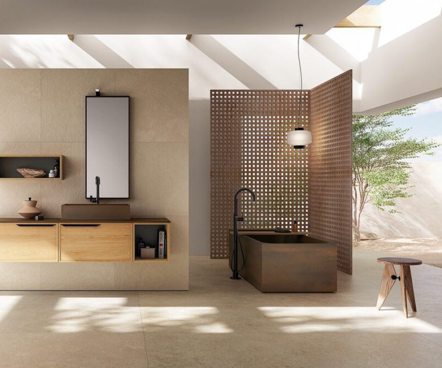 Arredo bagno con lavabo sospeso in legno chiaro, vasca freestanding scura e divisorio in mattoni forati.