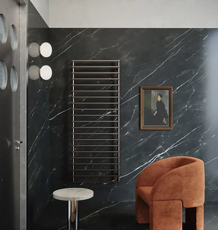 Radiatore orizzontale nero bronzato su parete effetto marmo scuro con poltrona arancione e tavolino moderno.