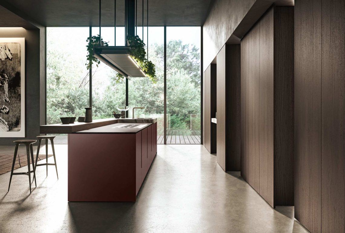 Cucina con isola bordeaux opaco e snack bar in legno, accostata a boiserie in legno scuro e grandi vetrate sul verde