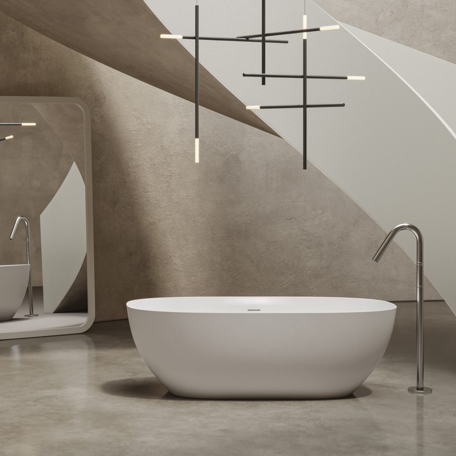 Vasca freestanding ovale bianca su pavimento in cemento, con lampade a sospensione e pareti inclinate grigio chiaro.