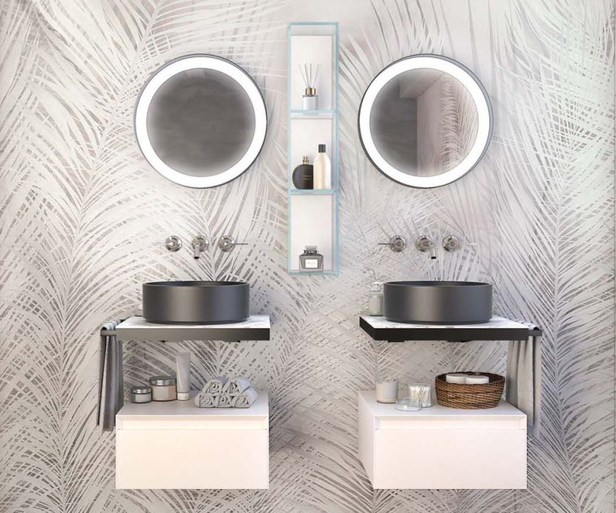Arredo bagno doppio con lavabi rotondi neri, specchi tondi retroilluminati e mobili sospesi bianchi su parete con decorazione fogliare.